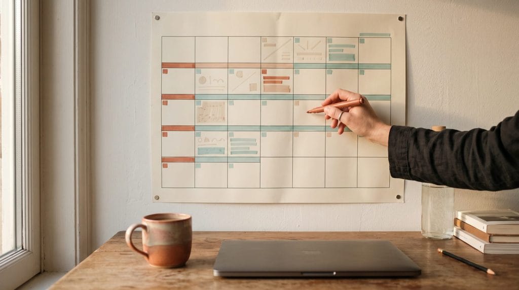 Hand marking a paper wall planner where some weeks are blocked in colour and other days are left deliberately blank